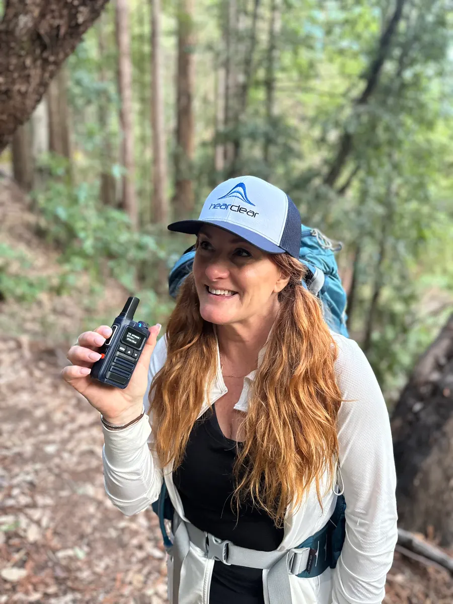 Hiker in a HearClear cap using a HearClear PTT radio on a forest trail
