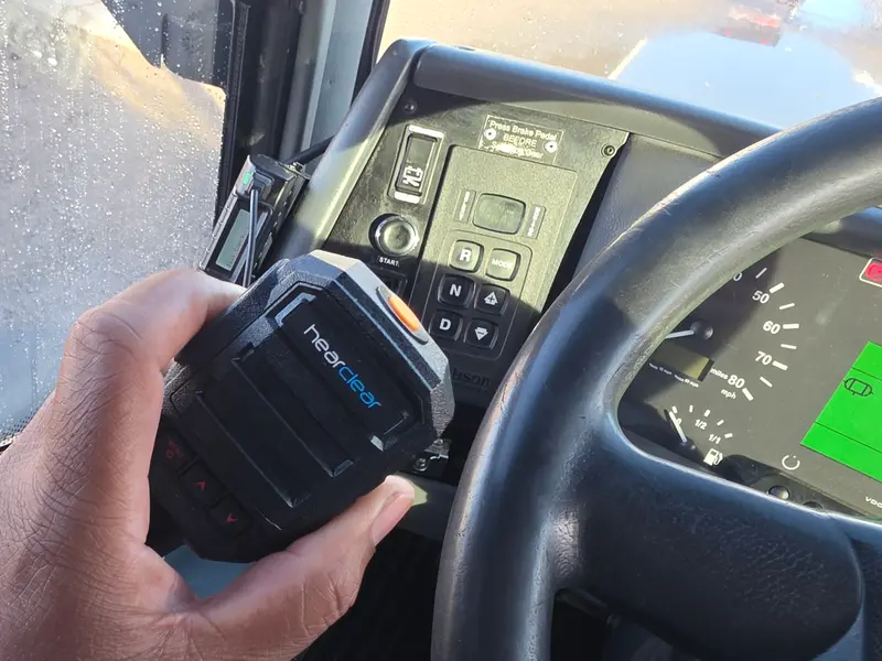 Driver holding a HearClear speaker mic beside the steering wheel